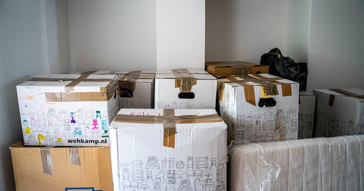 Stacked cardboard moving boxes wrapped in plastic, filling a bare room