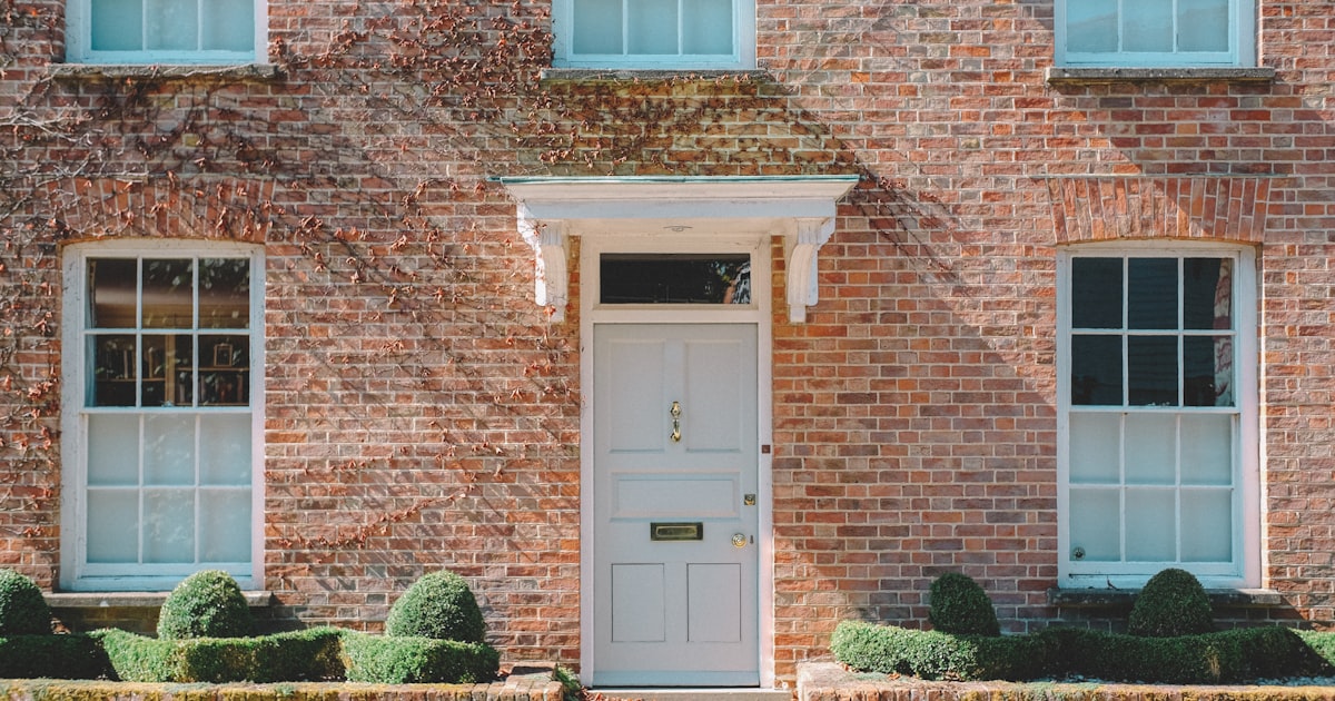 A red brick house with a pale front door, sash windows and clipped hedges either side of the path