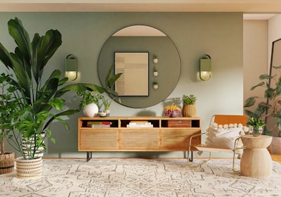 A green walled living space with large leafy plants, a round mirror and a wooden sideboard
