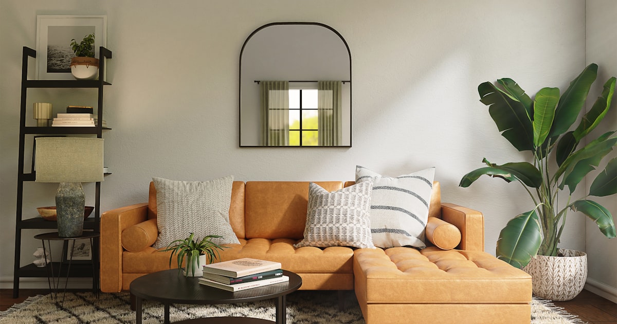 A tan sofa against a wall, with an arched mirror, open shelving and a large plant
