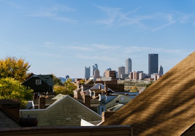 Rooftops of houses stepping downhill away from the viewer, with a city skyline in the distance beyond them