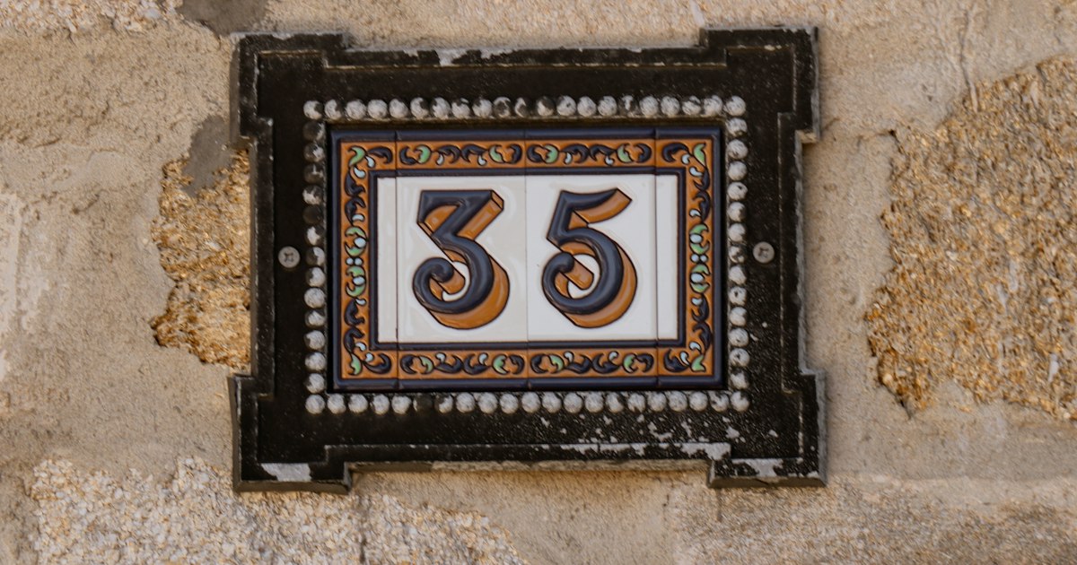 A ceramic house number 35 on a patterned orange and blue tile plaque, set into a weathered stone wall