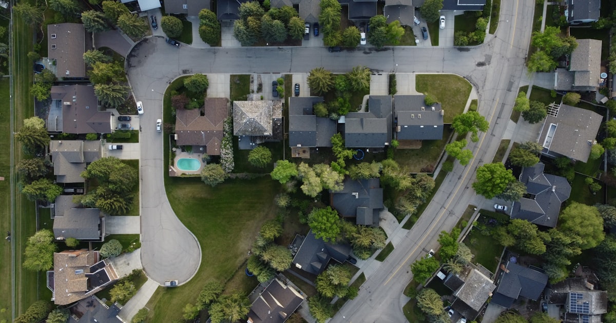 An overhead view of a suburban neighborhood, with a curved cul-de-sac on one side and a wider road running along the other